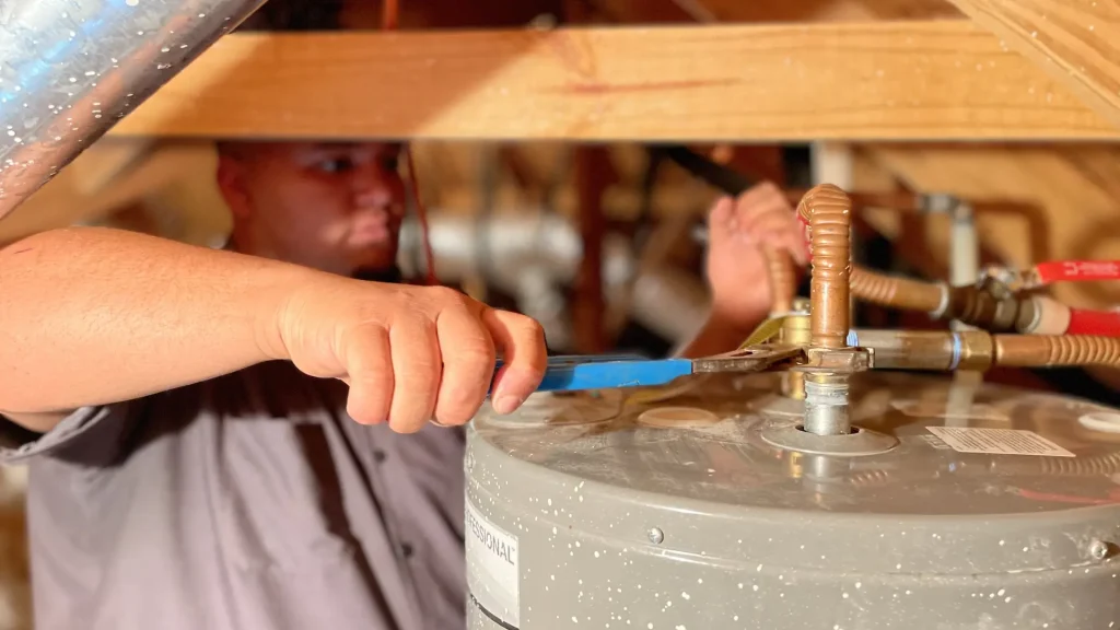 hero size zachary plumbing technician tighting water heater fittings in attic